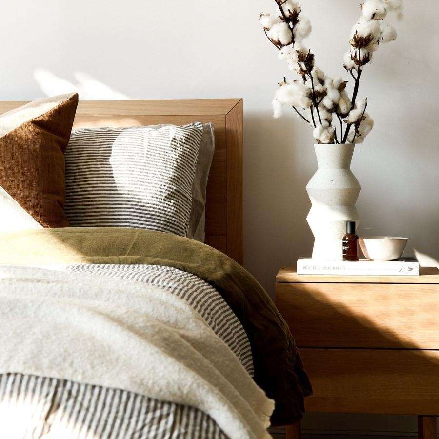 swath of sunlight shines across a well made bed and bedside table with a vase of cotton plants
